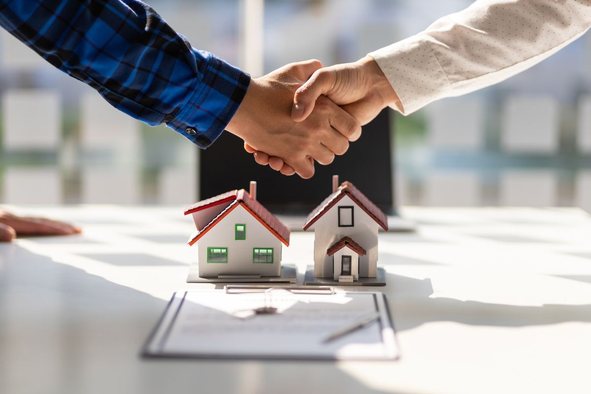 Poignée de main au-dessus de maquettes de maisons et d’un contrat